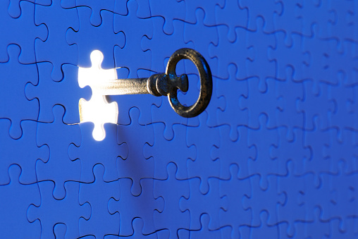 Inserting an antique skeleton key in a blue jigsaw puzzle against illuminated background.