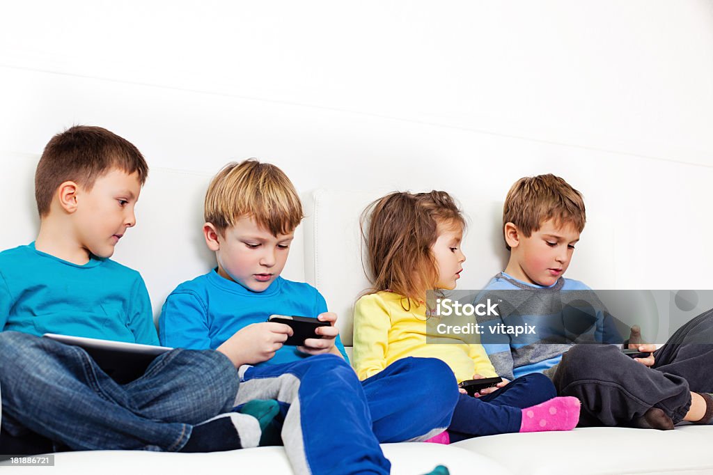 Children and technology Four children sitting on a couch using smartphones and a digital tablet. Boys Stock Photo