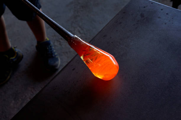 From above of anonymous glassmith putting blowpipe with hot melted glass on black table in dim light in workshop