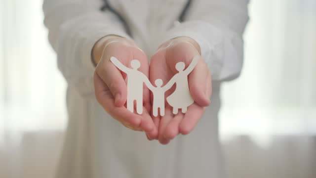 Close up of female doctor in white uniform with stethoscope holding paper family cutout icon, foster care, homeless support, protect, health care, world mental health day, support insurance concept