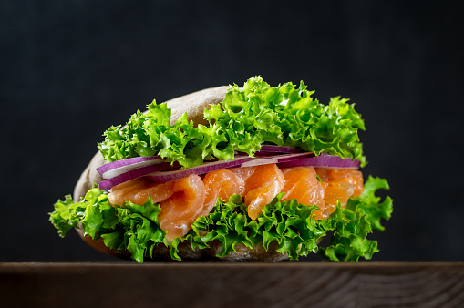Sandwich with fresh salmon, red onion and lettuce in a flavorful pita, on a cutting board on a dark background. Home cooking. Healthy fast food.