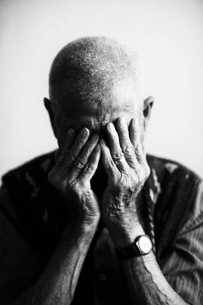 An old man covering his face with his hands in grief Old man holding face in hands. portrait of man holding head in agony black and white stock pictures, royalty-free photos & images