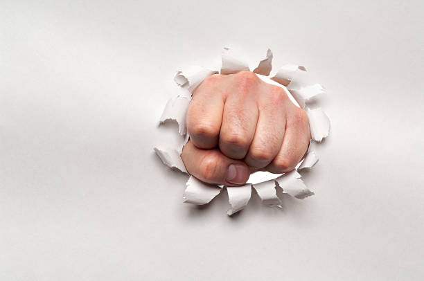 istock Fist punching through a ripped hole in a paper 181888886