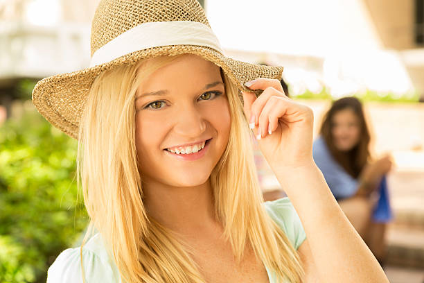 Fashion: Young adult outdoors in summer hat. Friends are in background.