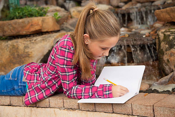 niños: hermosa chica primaria escribiendo en el cuaderno de la cascada - diary student lovelocal elementary age fotografías e imágenes de stock