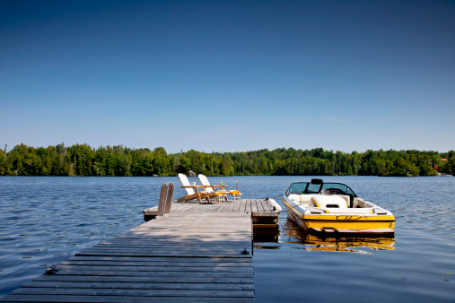 Two Adirondack chairs on Sunny Dock with Wakeboard boat. Horizontal.