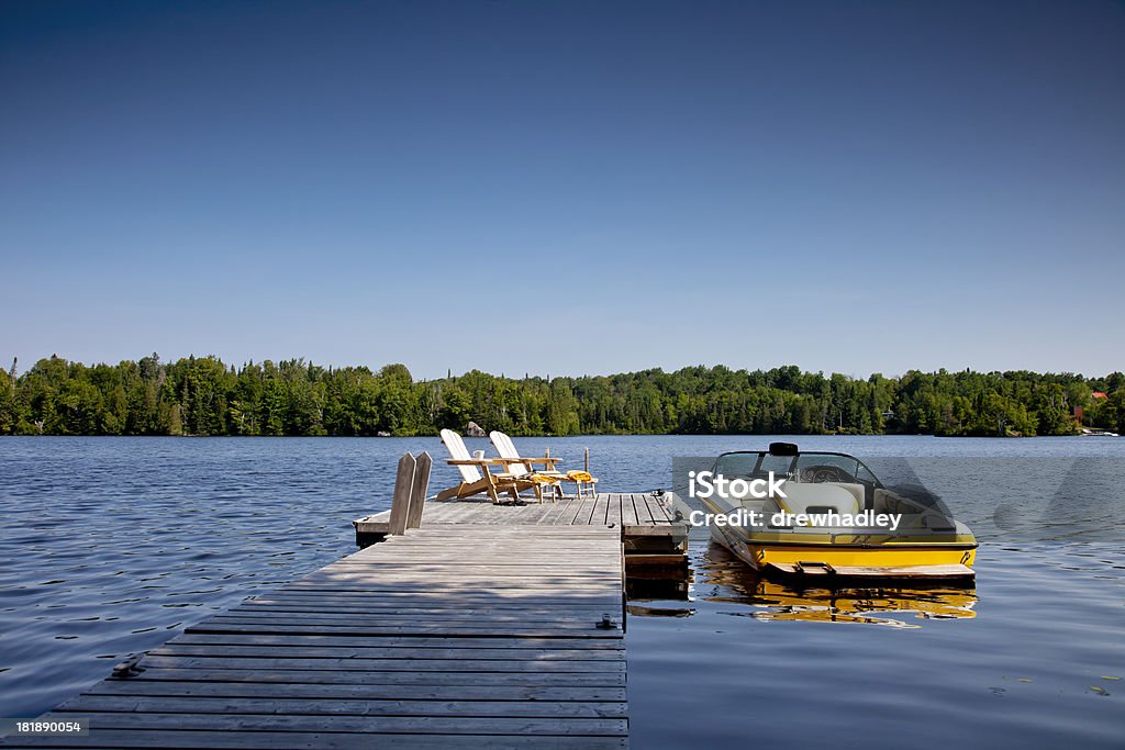 Wakeboard boat and Dock Two Adirondack chairs on Sunny Dock with Wakeboard boat. Horizontal. Lake Stock Photo