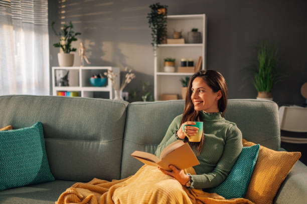 istock A woman is sitting on sofa at home, drinking tea and enjoying a book. 1818907833