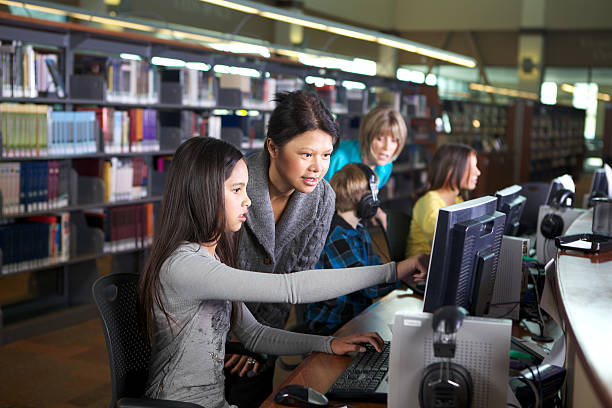 Librarian Working with Student on Computer at a Library A librarian is working with a young  girl on a computer work station. There are other children and another adult in the background.  Photo taken in a library at the Sacto'lypse. librarian stock pictures, royalty-free photos & images