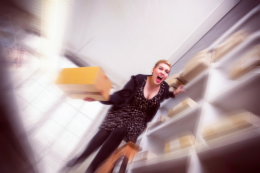 Office worker screams in sheer terror as she slips off a ladder with a box in her hand.