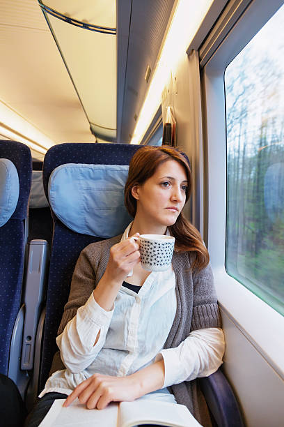 istock Young woman reading book and drinking coffee on train 181891283