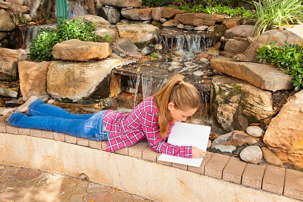 dzieci: piękny podstawowej dziewczynka pisania w notatniku przez wodospad. - diary student lovelocal elementary age zdjęcia i obrazy z banku zdjęć