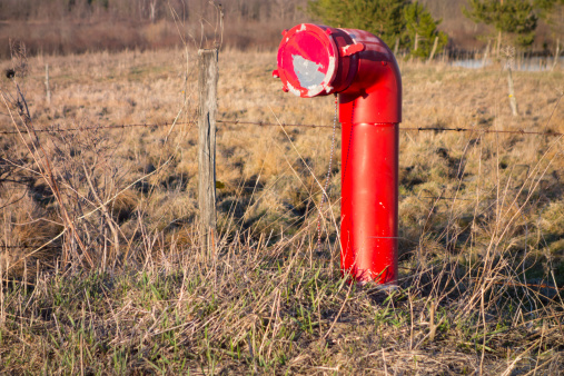 A bright red fire hydrant known as a dry hydrant in front of a barbed wire fence.