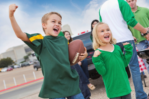 Excited kids tailgating with other fans at college football stadium.