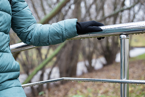 woman holding on to metal railing while climbing stairs in rainy weather. hand holding onto a metal handrail covered with raindrops.