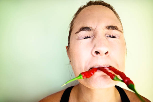 A young woman bites into a bunch of scarlet chili peppers and grimaces in horror at the burning heat!