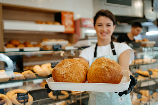 A close-up portrait captures a female mid-adult worker in a bakery, cradling freshly baked pastries, highlighting the dedication and skill that goes into each creation
