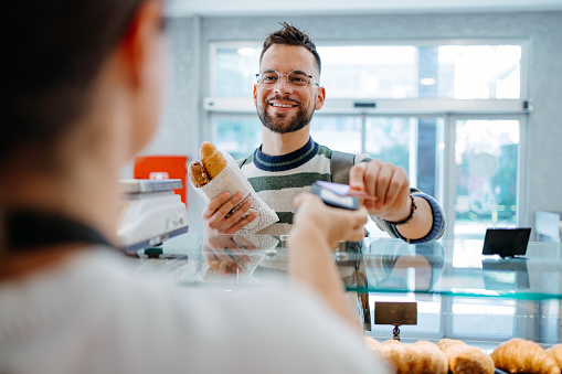 A close-up image captures a mid-adult female worker in a bakery, presenting pastries to a male mid-adult customer, creating a personalized and enjoyable shopping experience