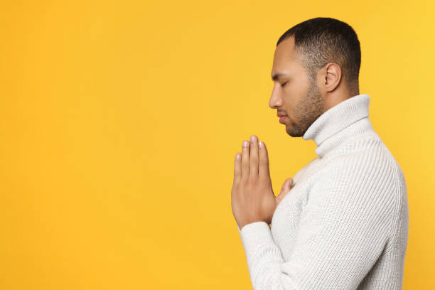 istock African American man with clasped hands praying to God on orange background. Space for text 1818940265