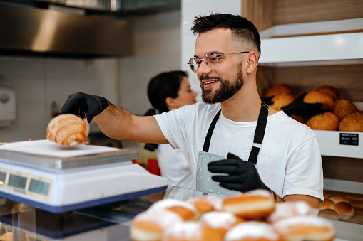 In this photo, a mid-adult man works behind the bakery counter, his genuine smile reflecting the joy he finds in creating and sharing delicious pastries with customers