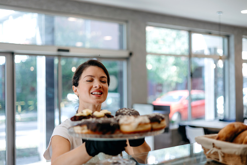 The mid-adult woman is captured holding a plate adorned with a delightful array of freshly baked donuts, showcasing her expertise in creating tempting treats that are sure to please every palate