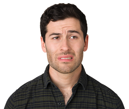 Portrait of bearded upset young man standing and looking at camera with dissatisfied sadness face, expressing sorrow, having bad mood. Indoor studio shot isolated on blue background.