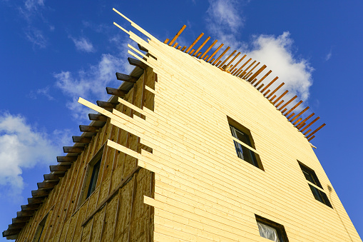 Residential house facade siding works with wooden planks after facade spraying with thermal insulation foam, blue sky background