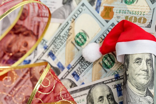 A hundred dollar roll in a Christmas Santa hat as a Christmas present. US 100 dollar bills background.