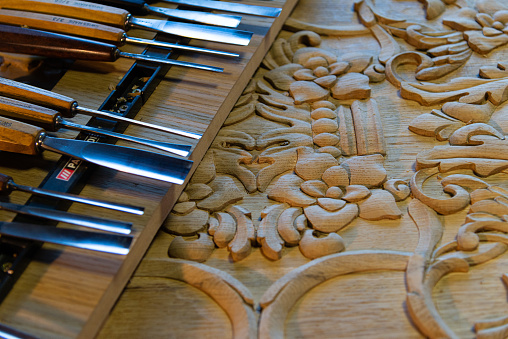 Close-up of a carved decoration on wood, with chisels, shallow depth of field in a workshop