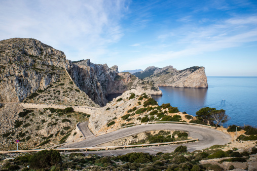 Western view over dramatic cliffs from the lighthouse at the very northern tip of Majorca on the beautiful Cap de Formentor peninsula. The narrow winding road leading to the lighthouse in foreground.