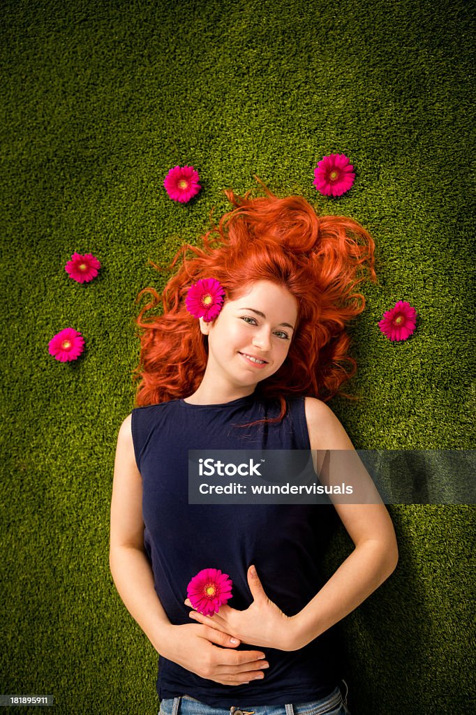 Redhaired girl lying on grass en el parque con flores - Foto de stock de Acostado libre de derechos
