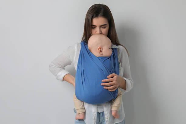 istock Mother holding her child in sling (baby carrier) on light grey background 1818959918