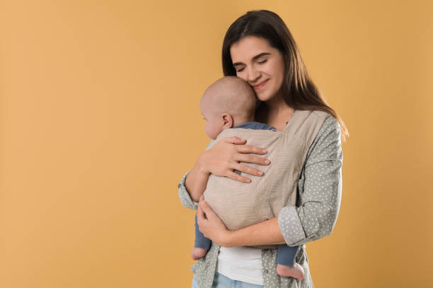istock Mother holding her child in sling (baby carrier) on beige background. Space for text 1818960477