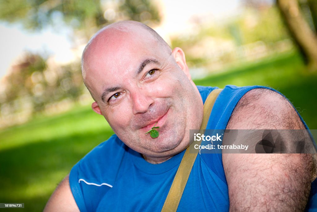 Happy Go Lucky happily smiling bald man / model with typical symbol for luck between his lips - the four-leafed clover. istockalypse barcelona.  Adult Stock Photo
