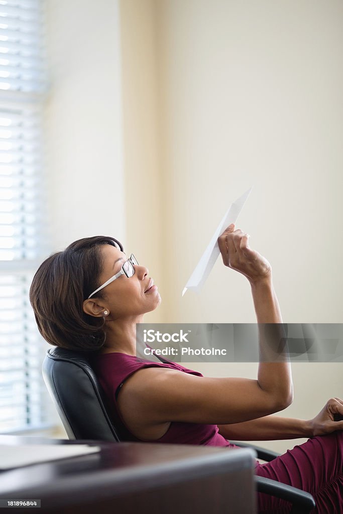 Businesswoman Throwing Paper Plane In Office Side view of mid adult businesswoman throwing paper plane in office Paper Airplane Stock Photo