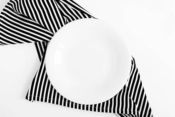 Empty white plate on a striped black napkin on the white background. Top view. Close-up. Copy space.