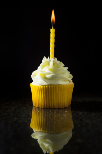 A lemon-lime cupcake with a birthday candle on a black granite countertop with a black background. Similar Images: