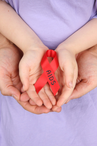 Child holding aids awareness ribbon with fathers's hands cradling hers.