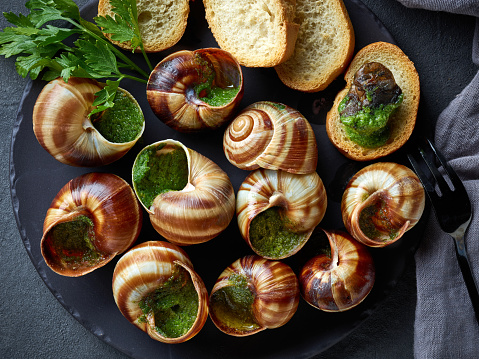 plate of baked escargot snails filled with parsley and garlic butter on grey background, top view