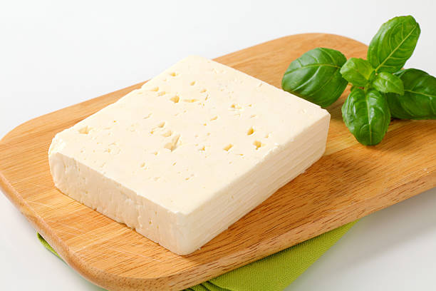 feta cheese block of feta cheese with a fresh basil on a wooden cutting board feta cheese block stock pictures, royalty-free photos & images