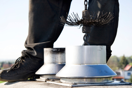 Close up of a chimney sweep on top of the chimney. Wearing the traditional workwear and holding a rope with the broom inside of the chimney. Clear sky in the background.