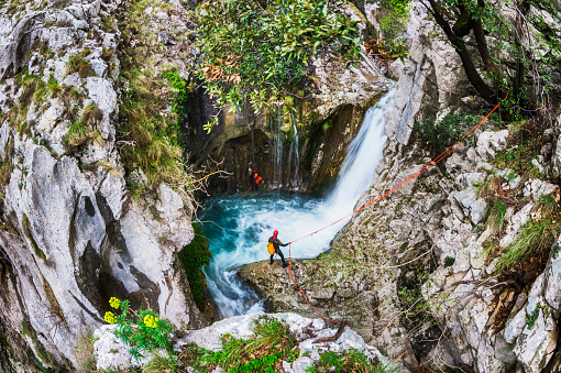 Members of canyoning team communicating by the waterfall while finding their way through the canyon.