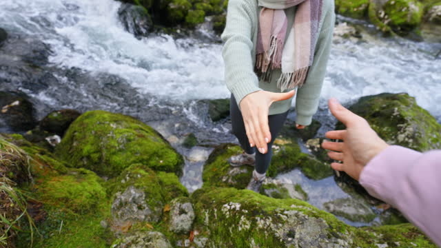 SLO MO Crop Hand Of Boyfriend Giving A Helping Hand to Woman Climbing Rocks Near Flowing River in Forest