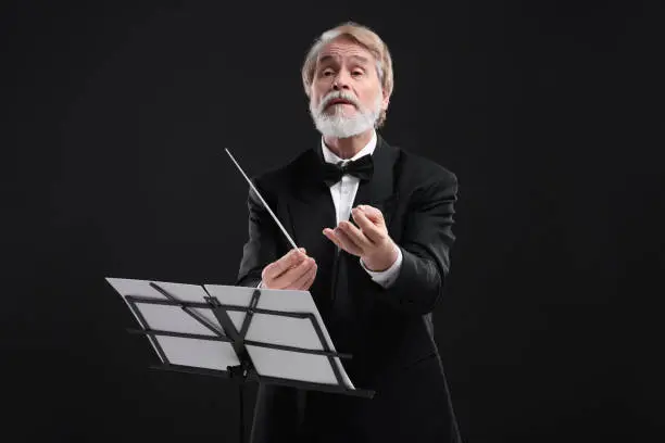 Photo of Professional conductor with baton and note stand on black background