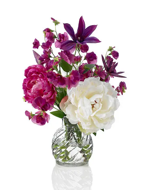 A beautiful springtime arrangement of flowers in a swirled glass vase. The bouquet contains peonies, clematis, and sweet peas. Shot against a bright white background. There is a path which may be used to delete the reflection if desired. Extremely high quality faux flowers.