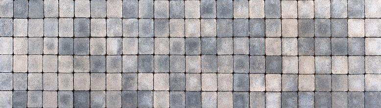 Sidewalk made of square paving stones in different beige and gray colors in panoramic close-up