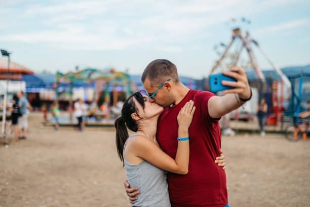 istock Young Couple Taking Selfies While Kissing In Amusement Park 1819075980