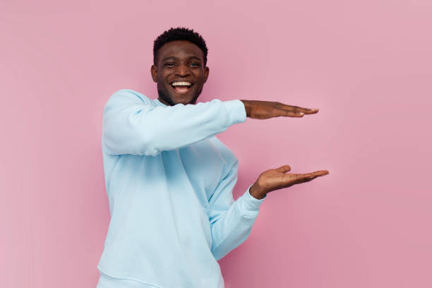 istock african american man in blue sweater holds empty space on pink isolated background, the guy shows the size 1819076542