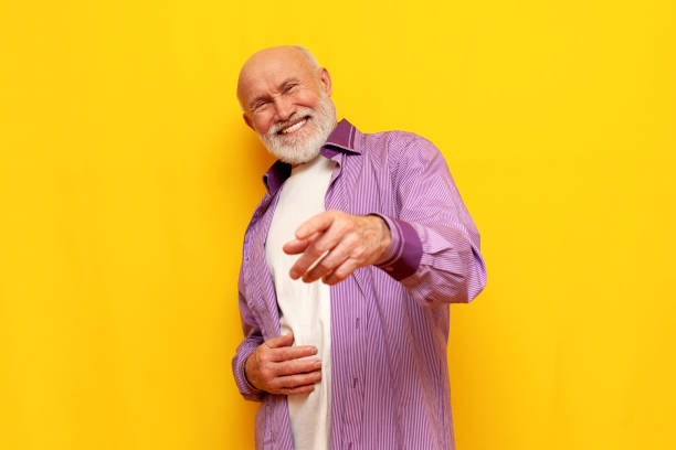 istock old bald grandfather with gray beard points forward and laughs on yellow isolated background 1819083385