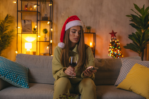 Sad young woman drinking wine at home during Christmas.